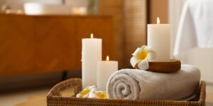Burning candles with flowers and towel on table in spa salon, cl